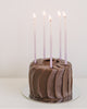 Tall hand-dipped violet color beeswax birthday candles with ombré effect on a small chocolate cake.