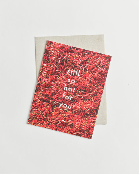 Photo greeting card of a bed of red chili peppers and white words “still so hot for you”.
