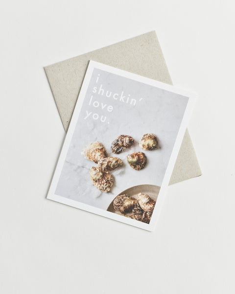 Photo greeting card of oyster shells scattered on a marble counter and words “I shuckin’ love you”