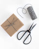 Spool of black and white baker’s twine next to a gift wrapped in kraft paper and tied with the twine in a bow